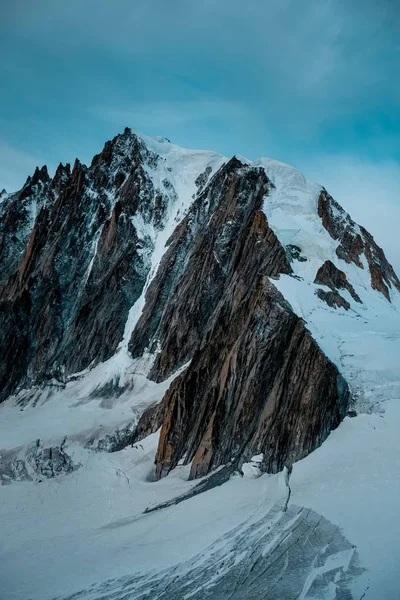 Tiro vertical de una montaña nevada con un cielo azul en el fondo — Foto de Stock