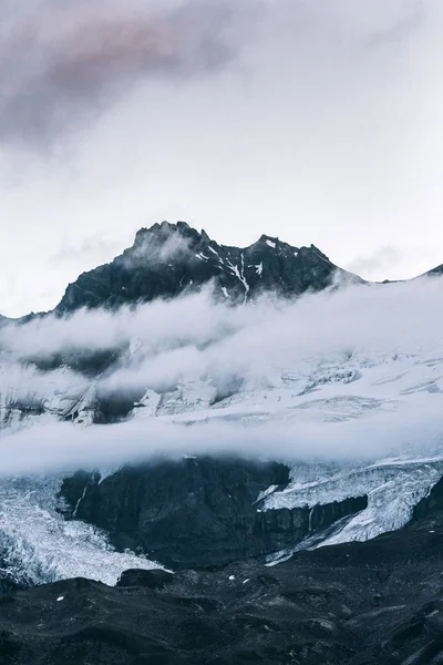 Vertikal bild av en snöig bergstopp ovanför molnen med en klar himmel i bakgrunden — Stockfoto