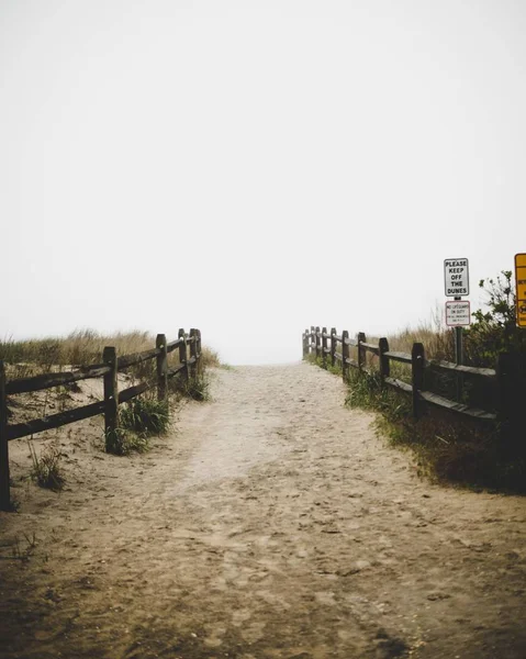 Tiro vertical de um caminho arenoso com grades de madeira nas laterais e céu branco claro perto da praia — Fotografia de Stock