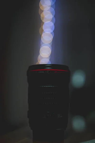 Vertical shot of a camera Lens with blurred lights in the background — Stock Photo, Image