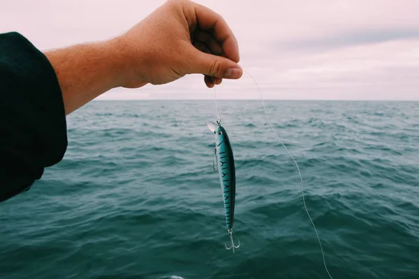 Κοντινό πλάνο ενός ατόμου που κρατά ένα δόλωμα για ψάρεμα με τη θάλασσα και ένα συννεφιασμένο ουρανό στο παρασκήνιο — Φωτογραφία Αρχείου