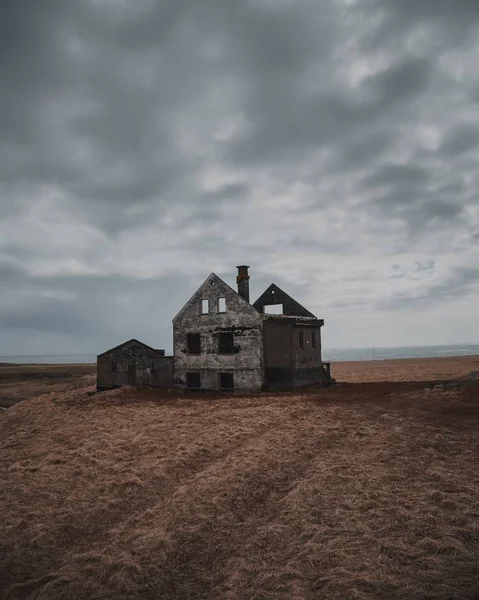 Piękne ujęcie starego opuszczonego i częściowo zniszczonego domu na dużym polach brązowych pod szarym niebem — Zdjęcie stockowe