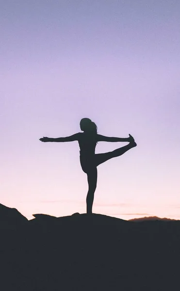 Силует підходящої жінки, що практикує йогу на високій скелі на заході сонця — стокове фото