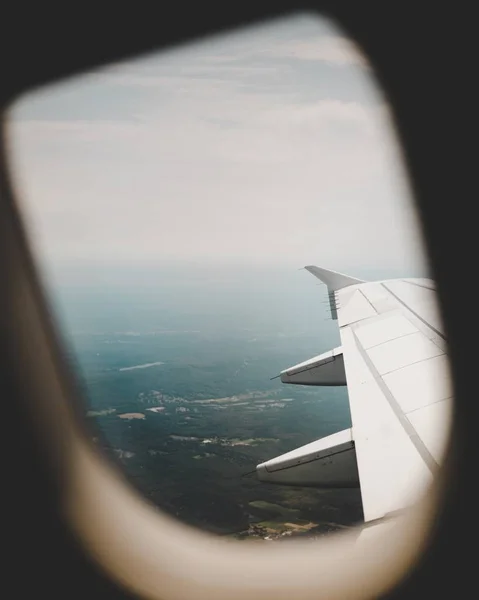 An airplane\'s window with the view of the green fields above and the right-wing