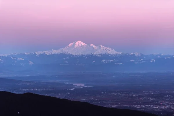 Belo tiro de um campo com uma montanha nevada na distância e um belo céu no fundo — Fotografia de Stock