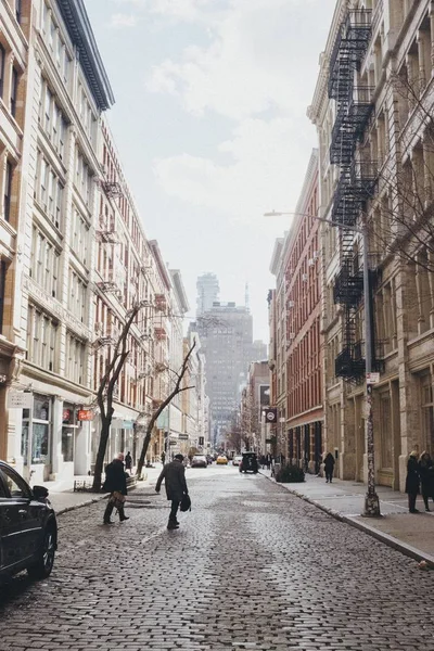 Tiro vertical de pessoas que cruzam uma estrada entre edifícios castanhos e brancos — Fotografia de Stock