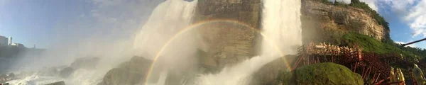 Foto panorámica de una cascada y un arco iris sobre ella con un cielo nublado en el fondo —  Fotos de Stock