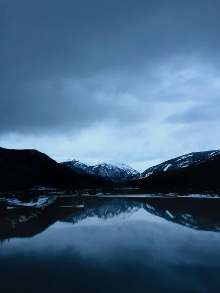 Tiro vertical de agua con montañas nevadas en la distancia bajo un cielo nublado —  Fotos de Stock