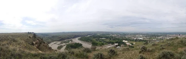 Foto panorámica de colinas cubiertas de hierba con edificios en la distancia bajo un cielo nublado —  Fotos de Stock