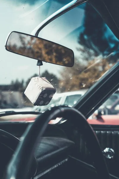 Vertical interior shot of a car with a dice hanging from a car's mirror and a blurred background — Stock Photo, Image