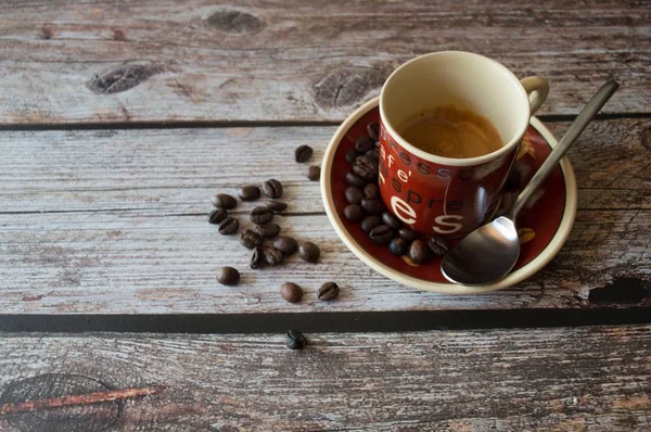 Foto aérea de una taza de café cerca de granos de café y una cuchara de metal en una superficie de madera — Foto de Stock