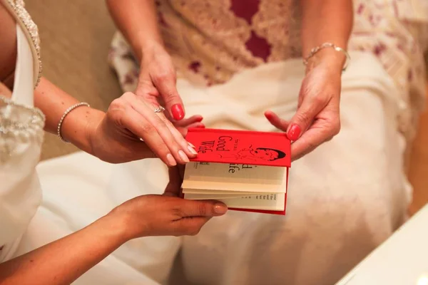 Selective closeup shot of two females wearing dresses and jewelry holding a small red book