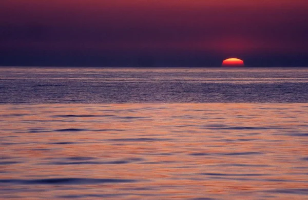 Tiro largo de um mar abaixo de um céu roxo durante o pôr do sol — Fotografia de Stock