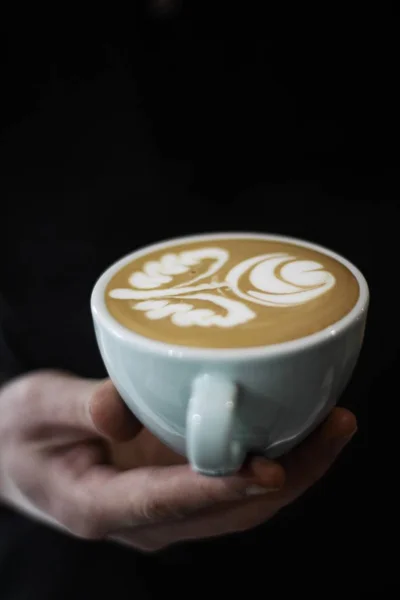 Vertikale selektive Nahaufnahme von Kaffee mit Latte Art in einer weißen Keramiktasse auf der Handfläche einer Person — Stockfoto
