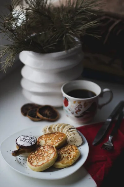 Pfannkuchen und in Scheiben geschnittene Bananen auf einem Teller neben einer Teetasse und einem Blumentopf auf einem Tisch — Stockfoto