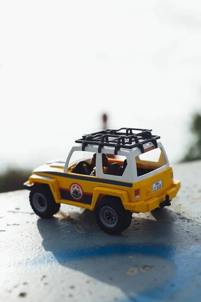 Close-up de um carro de brinquedo amarelo em uma superfície de concreto com um fundo borrado durante o dia — Fotografia de Stock