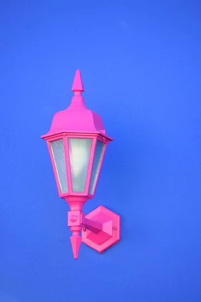 Tiro vertical de una lámpara de aplique rosa unida a una pared azul — Foto de Stock