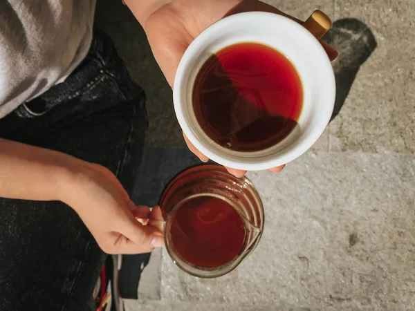 Režie osoby držící skleněný džbánek a bílý keramický šálek čaje — Stock fotografie