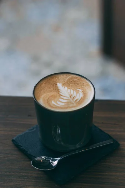 Zbliżenie kawy z Latte Art w niebieskim Kubek ceramiczny i łyżeczka na drewnianym stole — Zdjęcie stockowe