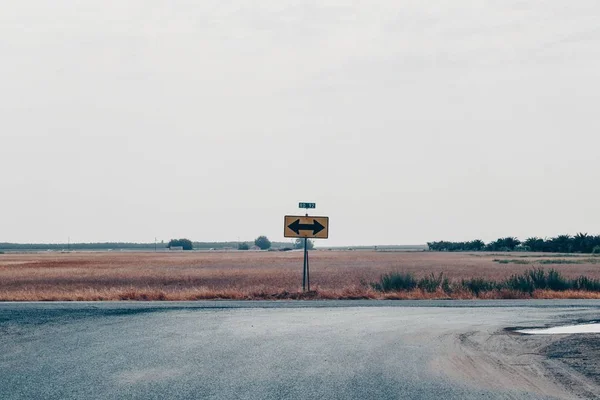Tiro largo de um sinal de estrada com uma seta preta apontando para ambos os lados — Fotografia de Stock