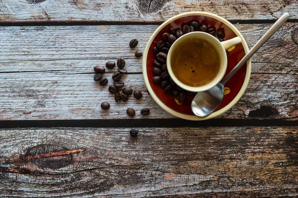 Накладний знімок чашки кави біля ложки та кавових зерен на дерев'яній поверхні — стокове фото