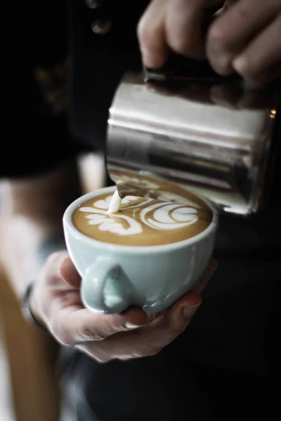 Eine Person gießt Milch in eine weiße Keramiktasse mit Kaffee mit Latte Art — Stockfoto