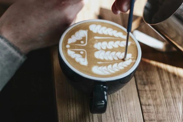 Selektive Nahaufnahme von Kaffee mit Latte Art in einer schwarzen Keramiktasse auf einer Holzoberfläche — Stockfoto