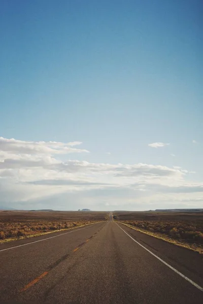 Tiro vertical de uma estrada vazia no meio de um deserto sob um belo céu azul — Fotografia de Stock