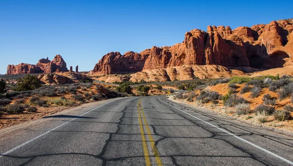 Hermosa toma de un camino vacío en medio de un desierto con arbustos y acantilados en la distancia —  Fotos de Stock