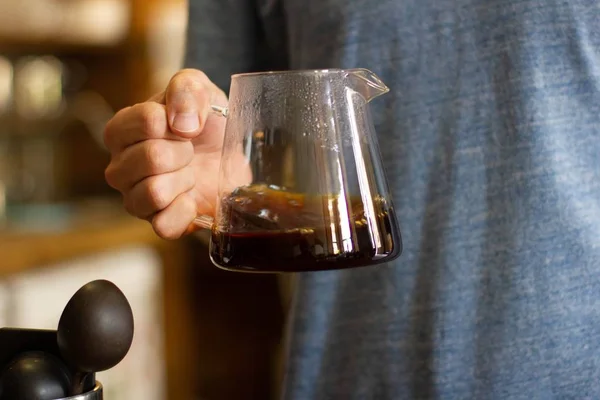 Amplio primer plano selectivo de una persona sosteniendo una jarra de vidrio llena de café — Foto de Stock