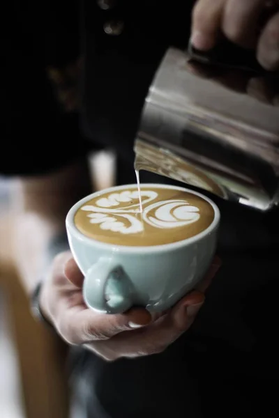 Vertikale selektive Nahaufnahme einer Person mit weißer Keramiktasse und Kaffee mit Latte Art — Stockfoto