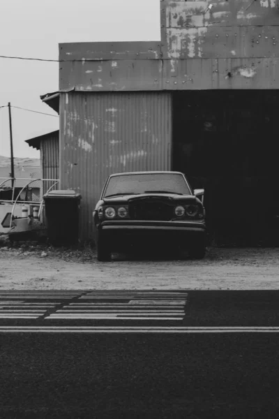 郊外の錆びたガレージの近くで古い放棄された車の垂直ショット — ストック写真