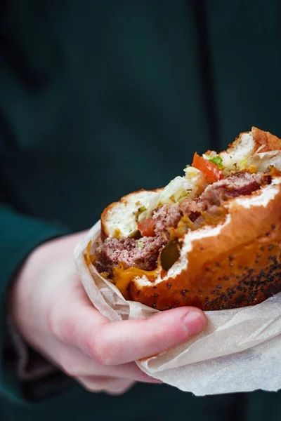 垂直选择性特写镜头的人拿着一个包裹的咬汉堡 — 图库照片