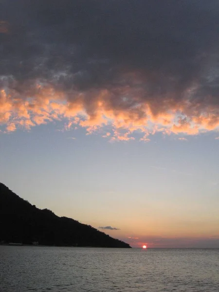 Plan vertical d'une montagne au bord de la mer sous un ciel nuageux au coucher du soleil — Photo