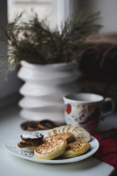 Pfannkuchen und in Scheiben geschnittene Bananen auf einem Teller neben einer Teetasse und einem Blumentopf auf einem Tisch — Stockfoto