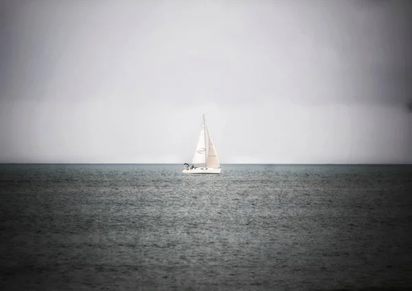Біла одиночна яхта посеред спокійного моря з сірими дощовими хмарами на задньому плані — стокове фото