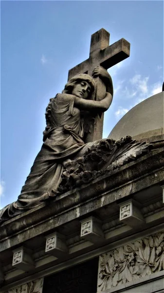 Nízký úhel záběru ženské sochy objímající kříž na střeše budovy — Stock fotografie