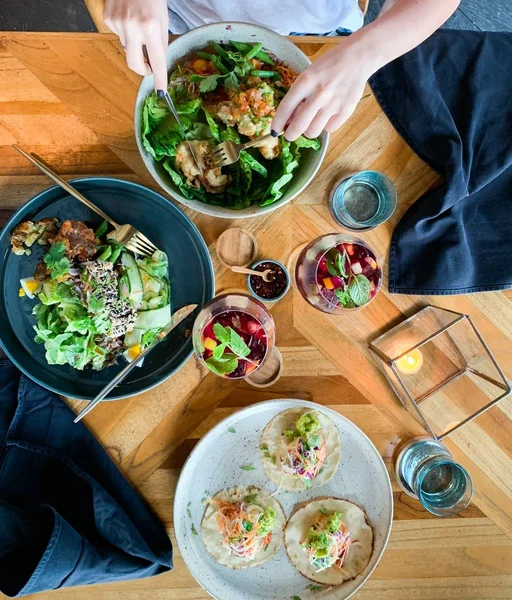 Накладний знімок людини, що їсть органічні салати біля столу, наповненого окулярами з фруктовим коктейлем — стокове фото