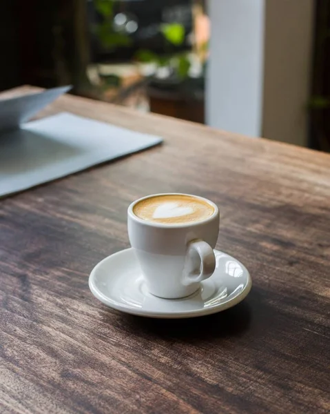 Closeup vertical tiro de café com arte latte em um copo de cerâmica branca em uma superfície de madeira — Fotografia de Stock