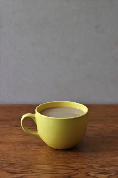 Tiro vertical de um café em uma xícara amarela em uma superfície de madeira com um fundo branco — Fotografia de Stock