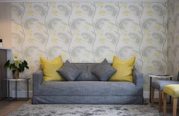 Interior shot of a house with a gray couch and a wall with leaf patterns