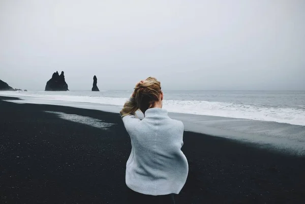 Donna seduta sulla riva vicino all'acqua con un cielo nuvoloso sullo sfondo girato da dietro — Foto Stock