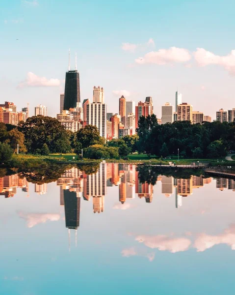 Imagen vertical distante del reflejo de edificios de gran altura y árboles en un lago bajo un cielo azul — Foto de Stock