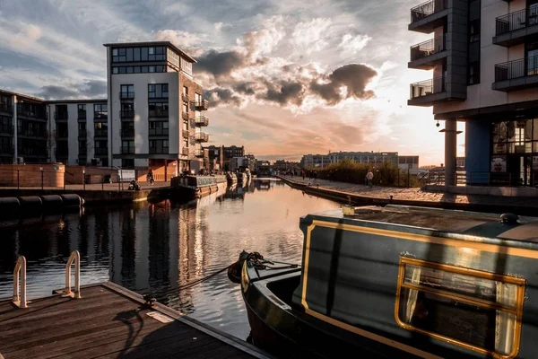 Amplio tiro de barcos cerca de un muelle en el cuerpo de agua rodeada de edificios durante la puesta del sol —  Fotos de Stock