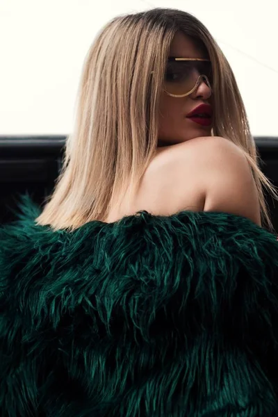 Vonzó női modell zöld prémes ruhában és arany keretes napszemüvegben. — Stock Fotó