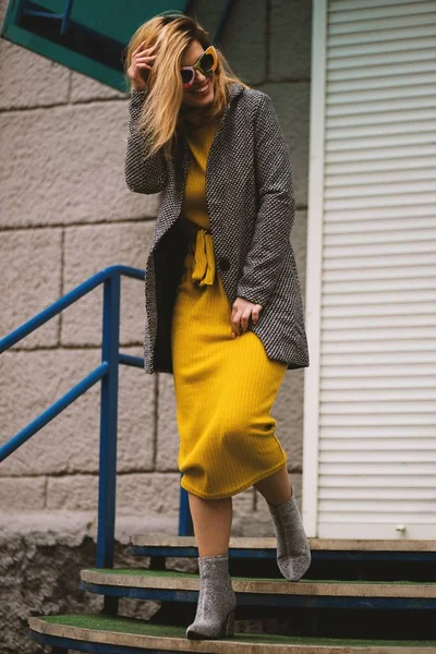 Vertikální záběr atraktivní usměvavé modelky ve žlutých šatech a kabátě na schodišti — Stock fotografie