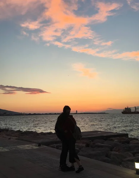 Foto vertical de un par de personas de pie sobre una carretera junto al mar durante la puesta de sol — Foto de Stock