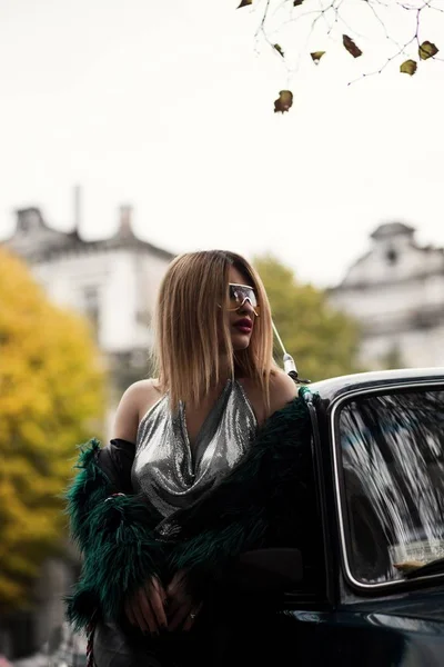 Tiro selectivo vertical de un atractivo modelo femenino elegante y de moda en un vestido cerca de un coche — Foto de Stock