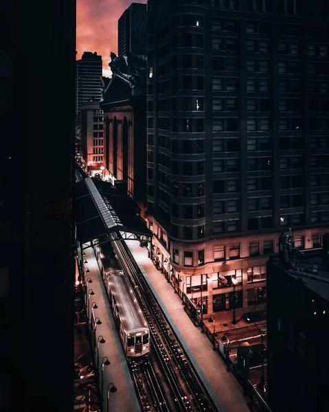 Vertical shot of a train on a rail near buildings in a city during dawn — ストック写真