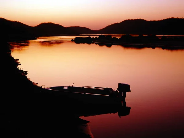 Силуэт катера на теле озера, окруженного горами во время заката — стоковое фото